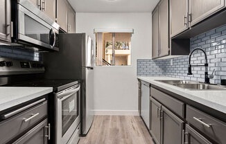 White tiled kitchen with stainless steel oven, microwave, and fridge..