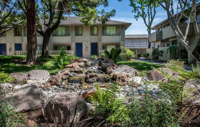 A stream of water flows through rocks in a garden at The Woods Apartments, San Jose, California