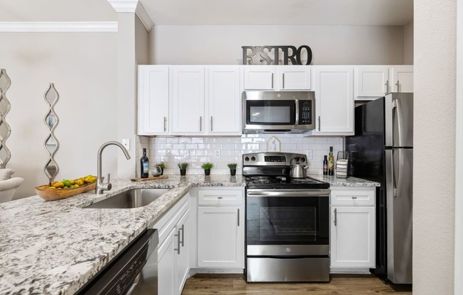 a white kitchen with stainless steel appliances and granite counter tops