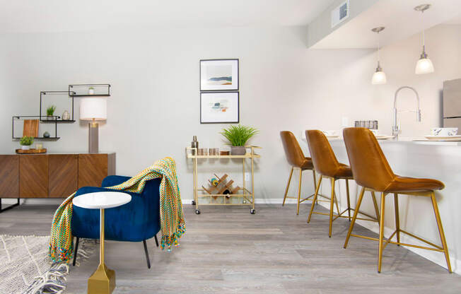 a living area with a blue chair and a kitchen with a bar table and chairs