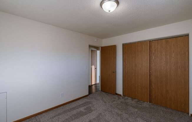 an empty living room with a carpeted floor and two wooden doors. Fargo, ND North Manor Apartments