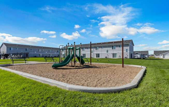 A playground with a green slide and a sandbox in the foreground.
