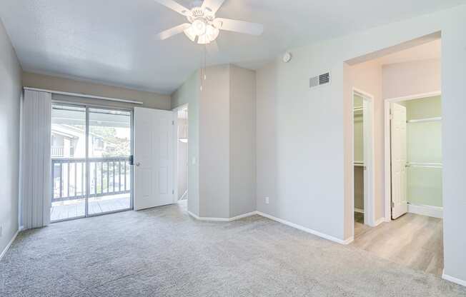 an empty living room with a ceiling fan and a door to a balcony