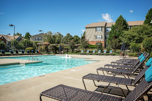 A pool with chairs around it and a building in the background.