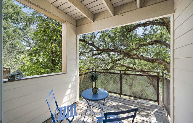 a small table and two chairs sit on a balcony with trees in the background