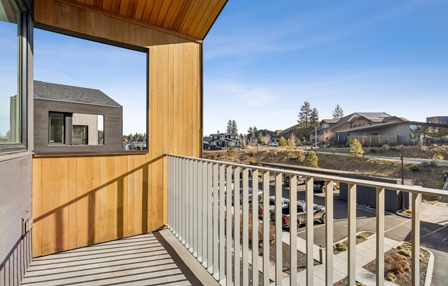 A balcony with a wooden railing and a view of a parking lot and buildings.