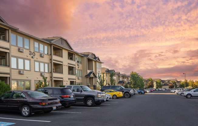 a city street with cars parked in front of an apartment building at sunset