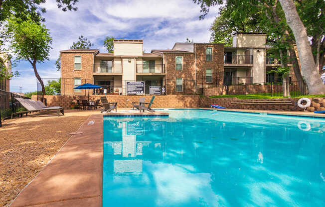 A swimming pool in front of a multi-story apartment building at Canyon Creek Apartments in the Dallas Midtown neighborhood of Dallas, TX.