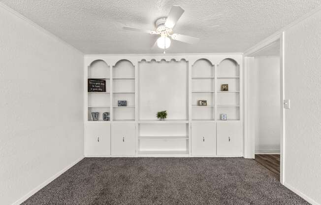 a living room with white shelves and a ceiling fan