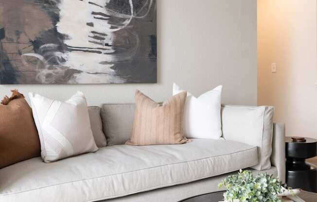A living room with a white couch and a large abstract painting above it.