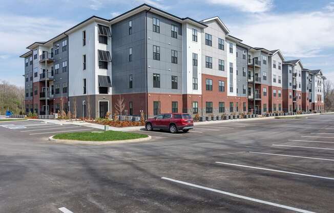 A red car is parked in a parking lot in front of apartment buildings.