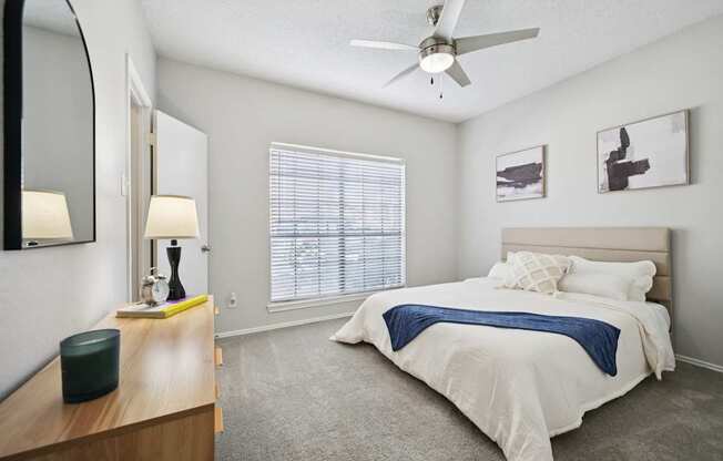 A bedroom with a bed, a dresser, a ceiling fan, and a window with blinds.