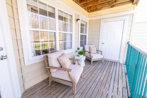 the front porch of a home with two chairs and a table