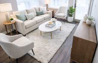 A modern living room with a white couch, a white rug, a wooden coffee table, and a white chair.