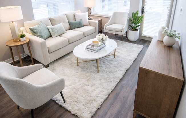 A modern living room with a white couch, a white rug, a wooden coffee table, and a white chair.
