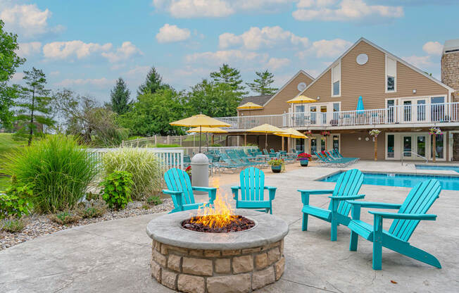 a fire pit with blue adirondack chairs and umbrellas in front of a
