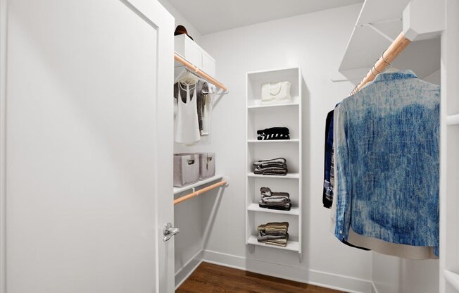 a small walk in closet with white shelves and a white door