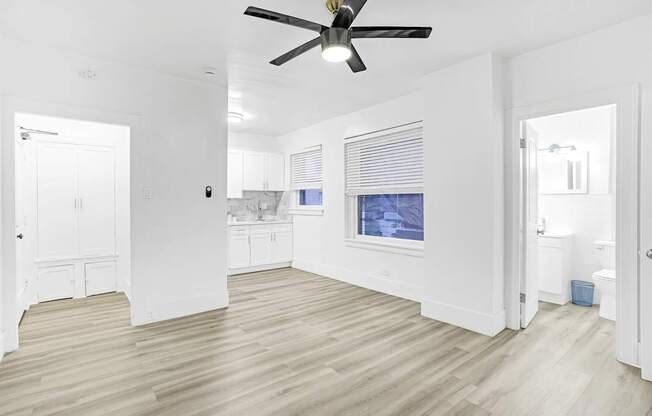 A room with a ceiling fan and light, wooden floors, and a window with blinds.
