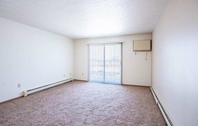 A room with a carpeted floor and a window with blinds.