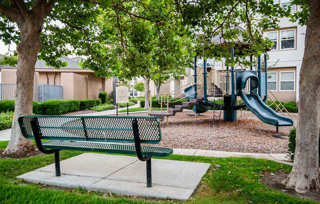 A green park bench sits in front of a playground.