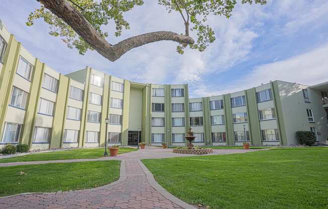 a courtyard in front of an apartment building with green grass and a tree