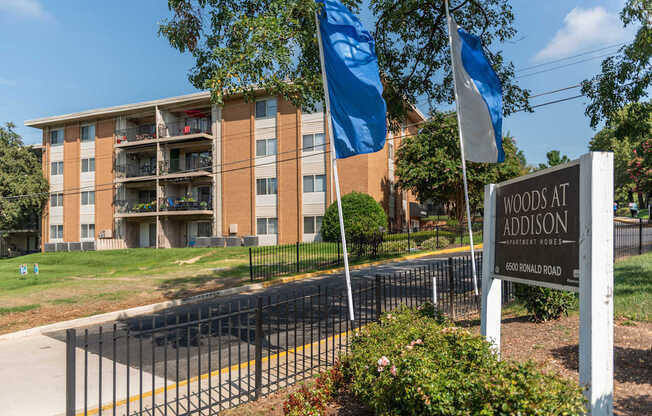 A sign for Woods at Addison stands in front of a building.