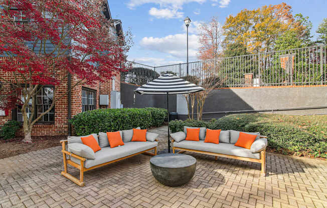 Two orange cushions on a grey sofa in a courtyard.
