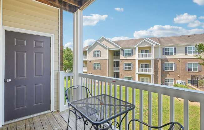 A balcony with a table and chairs overlooks apartment buildings.