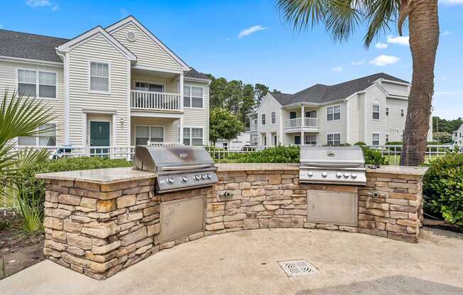 A stone wall with two built-in BBQs in front of a two-story apartment building.