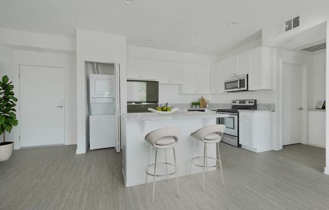 a kitchen with white cabinets and a bar with two stools