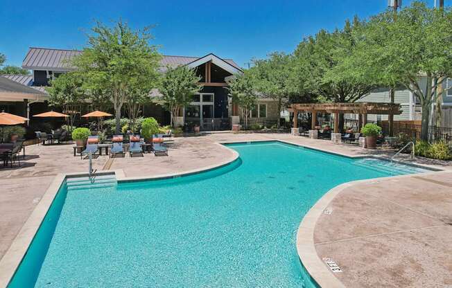 A large outdoor swimming pool surrounded by a patio area with chairs and umbrellas.