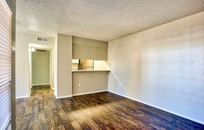 an empty living room with wood flooring and a kitchen