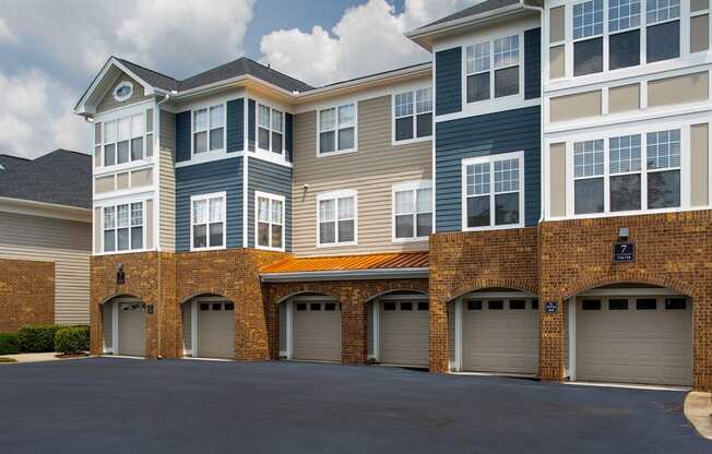 Luxury Apartments in Chapel Hill, NC, with In-Unit Washers and Dryers - The Reserve at Meadowmont - Property Exterior with Blue and Tan Walls, Stone Details, White Trim, Beige Attached Garages, Large Windows, and Manicured Hedges.