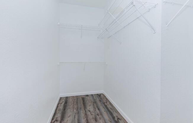 A minimalist empty closet with white walls, wooden flooring, and wire shelving on two sides, creating an organized and spacious appearance.