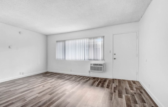 the living room of an apartment with wood flooring and a window