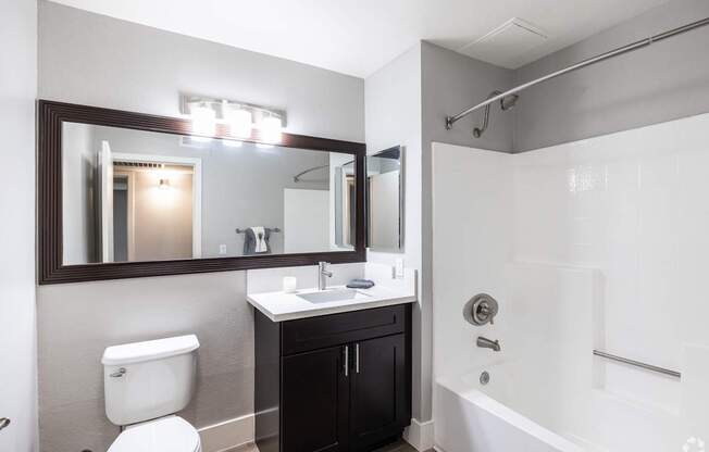 A bathroom with a toilet, sink, mirror, and bathtub.