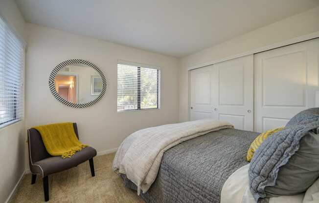 Master Bedroom with gray comforter. Room has Carpet, Gray Chair in corner, large closet with 3 doors and Window