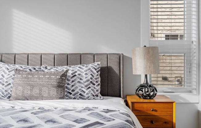 a bedroom with a bed and a dresser with a lamp and a window