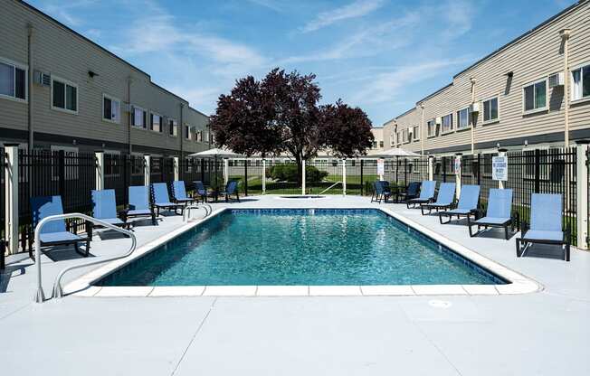 A swimming pool surrounded by chairs and a tree in a sunny courtyard.