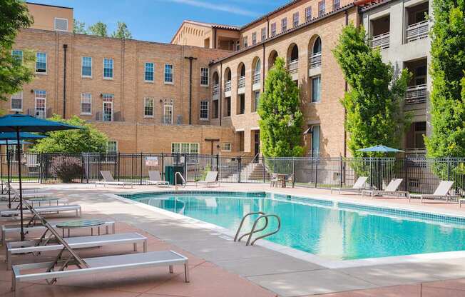 A pool surrounded by lounge chairs and trees in front of a building.