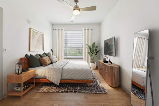 A bedroom with a bed, a nightstand, a plant, and a television at The Waterford At Rocketts Landing Apartments, PRG Real Estate, Richmond, Virginia