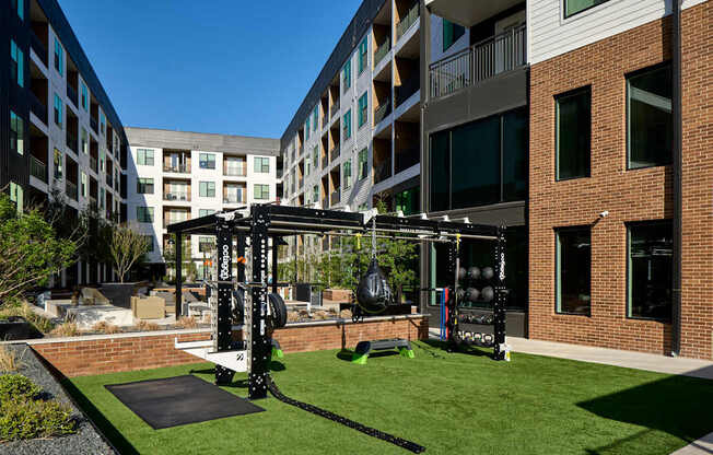 A gym is set up on a grassy area in front of apartment buildings.