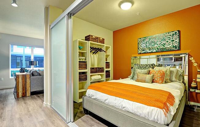 A bedroom with a bed, orange walls, and a sliding door leading to a balcony. at Kirkland Crossing Apartments, Kirkland, WA