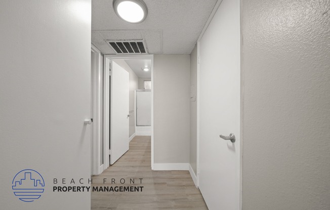 a renovated hallway with white walls and wood flooring and a door to a closet