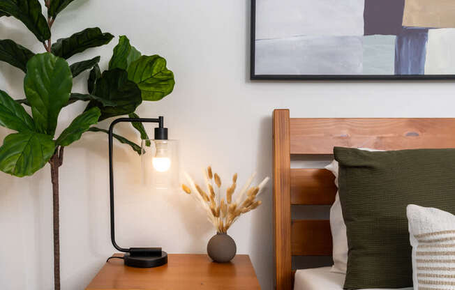 A modern bedroom with a wooden headboard and a side table with a lamp and a plant.
