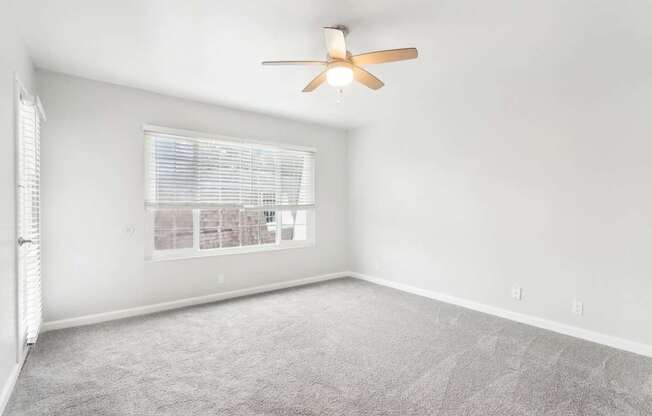 A room with a ceiling fan and a window with blinds.