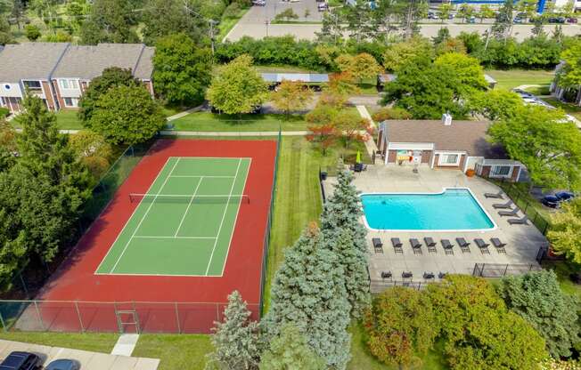 an aerial view of a tennis court and a swimming pool in a backyard with trees