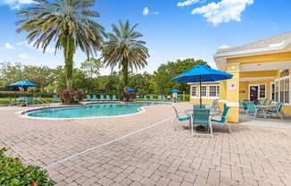 A pool area with a yellow building and palm trees.