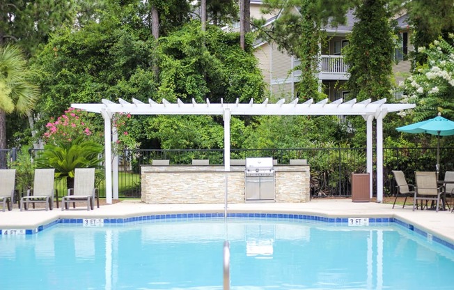 an outdoor kitchen next to a pool with a pergola