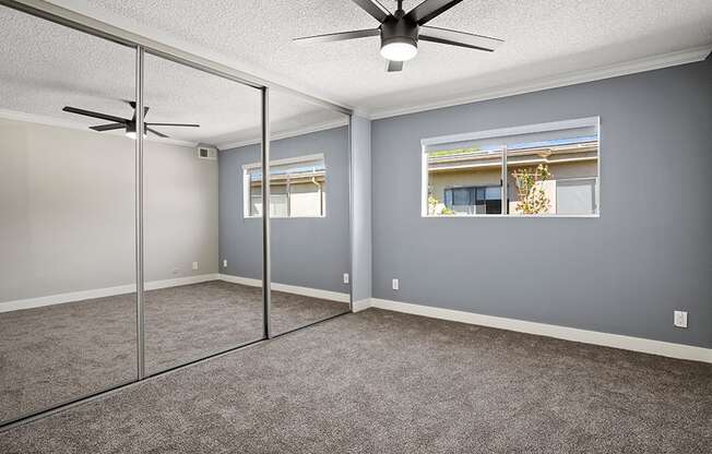 Carpeted bedroom with ceiling fan and large mirrored closet.